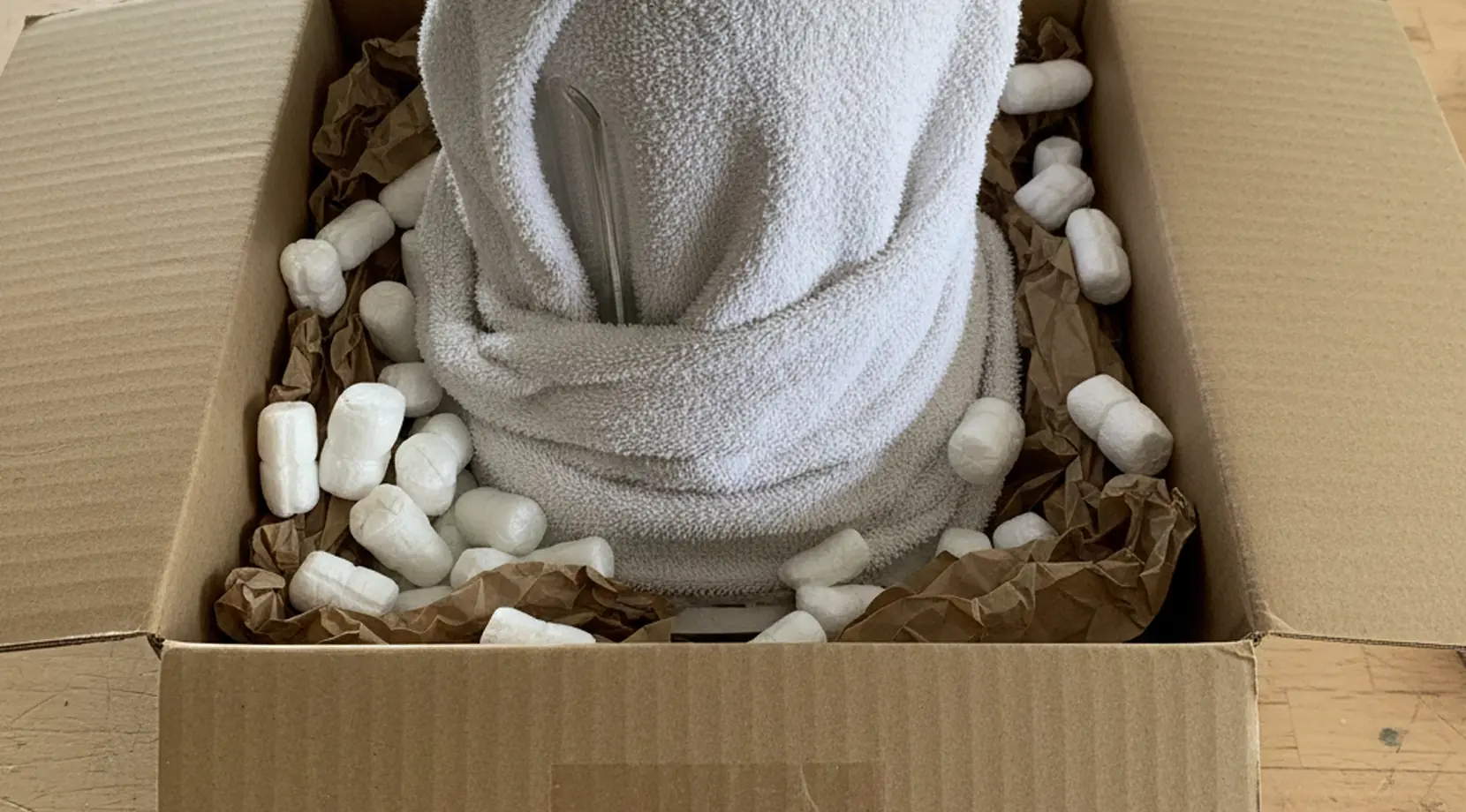 Fragile item wrapped in a towel inside a box with packing paper and peanuts, showing packing tips for a long distance move to prevent breakage.
