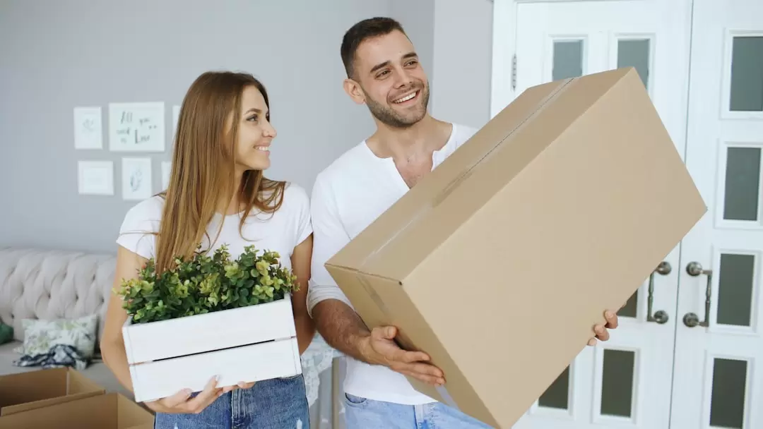 Smiling couple carrying cardboard boxes and household items while moving into a new home.