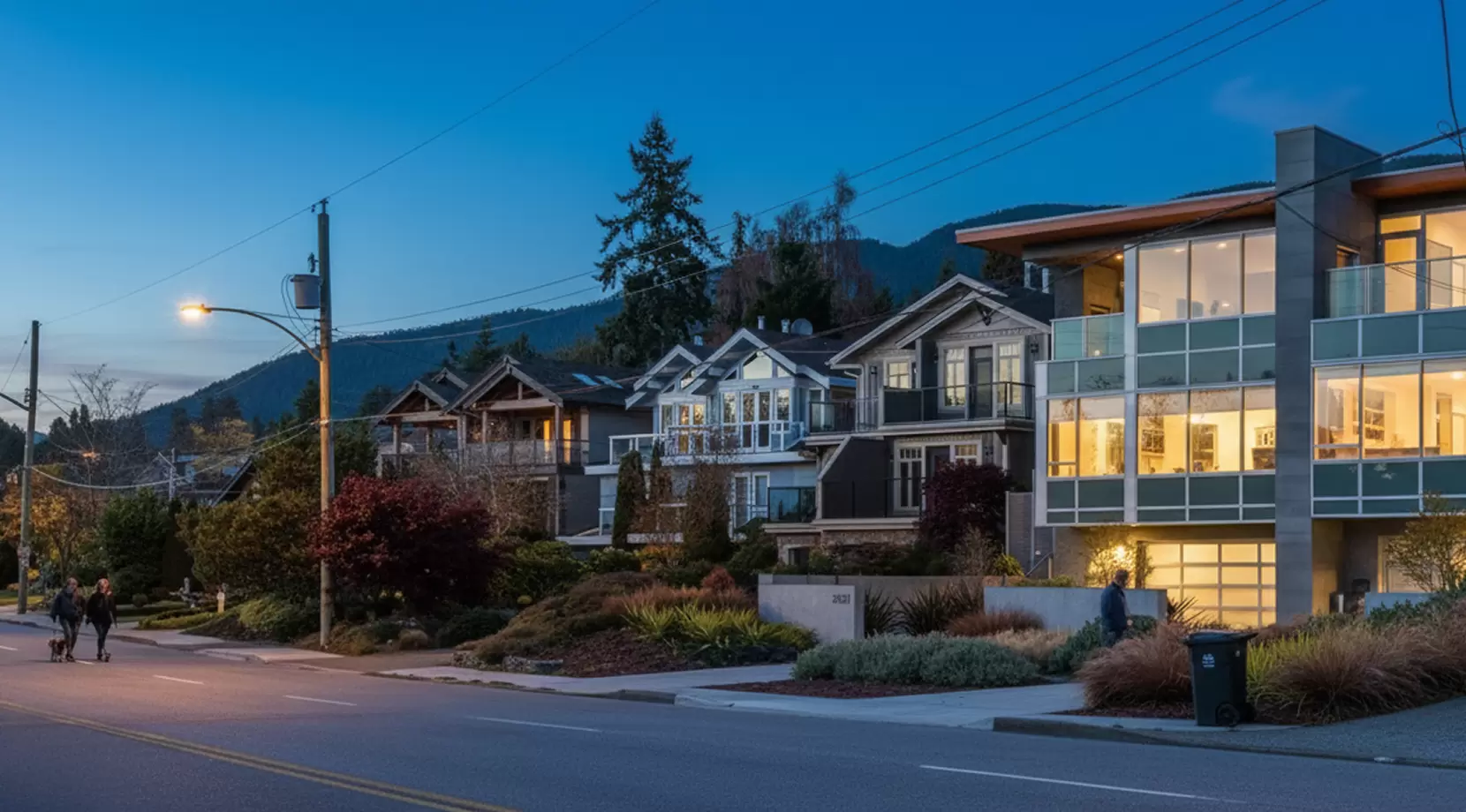 Evening street view of quiet residential homes with lights on and mountains behind, illustrating Living in West Vancouver safety and calm neighborhoods.
